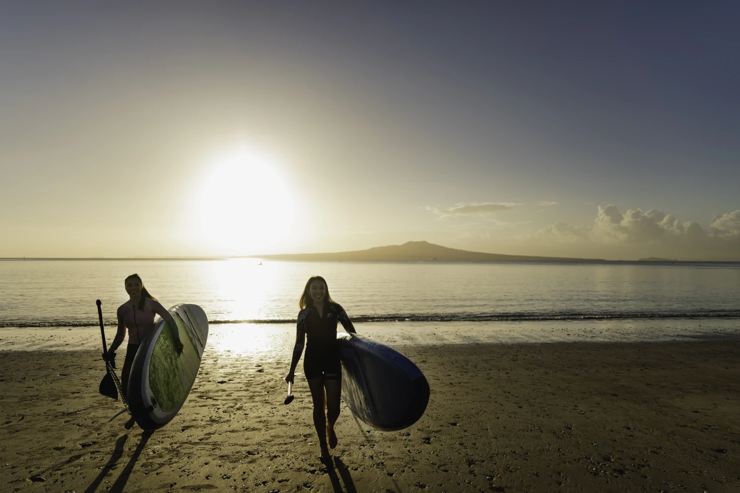 Two friends paddleboarding with Rangitoto in the backdrop
