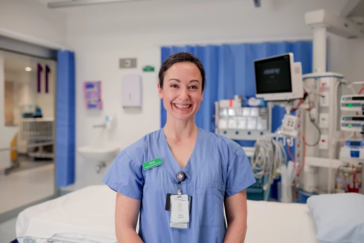 Critical Care Nurse Alicia standing in scrubs in front of a vacant ICU bed.