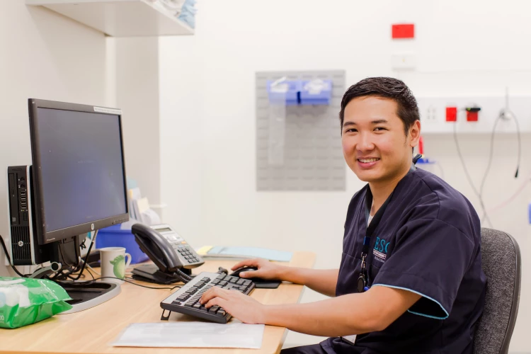 An Elective Surgery Centre nurse sitting at his desk typing on the keyboard.