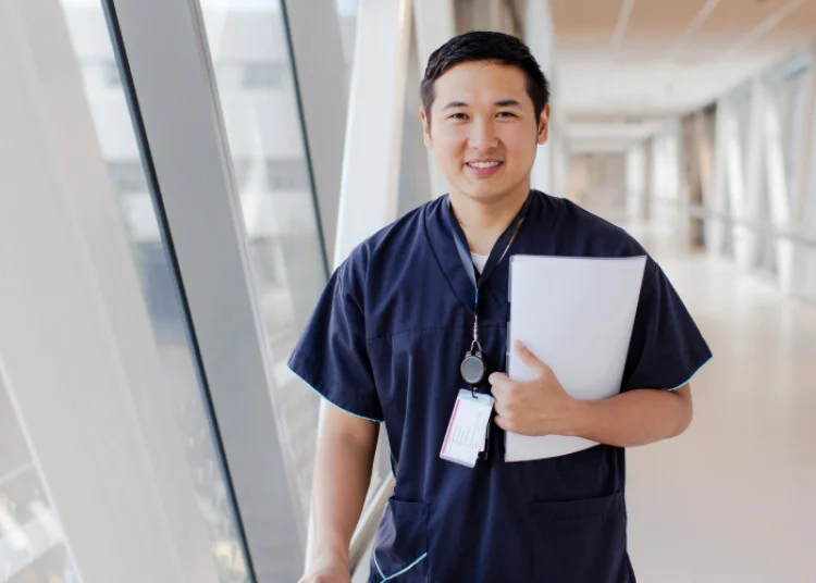 An ESC nurse standing in a brightly lit hospital corridor holding some paperwork.