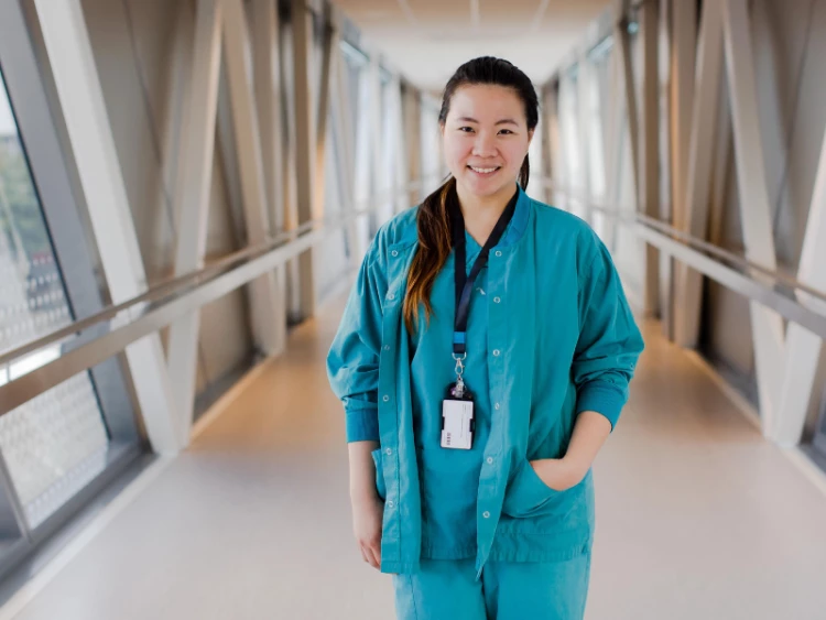 A Health New Zealand healthcare professional stands in the middle of a corridor smiling