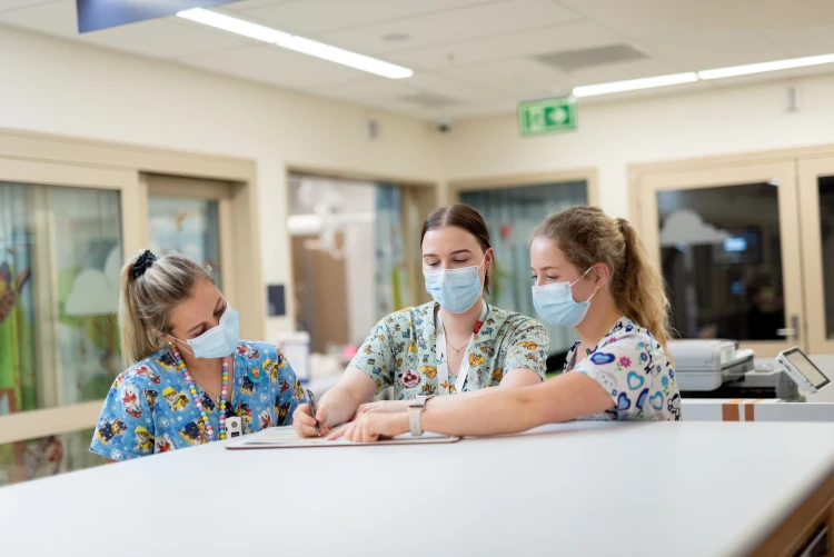 Three paediatric nurses congregating over patients records on the table at the nurses' station