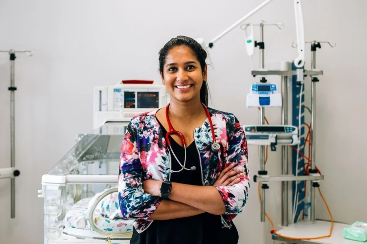 A Resident Medical Officer stands smiling with her arms crossed in front of an incubator