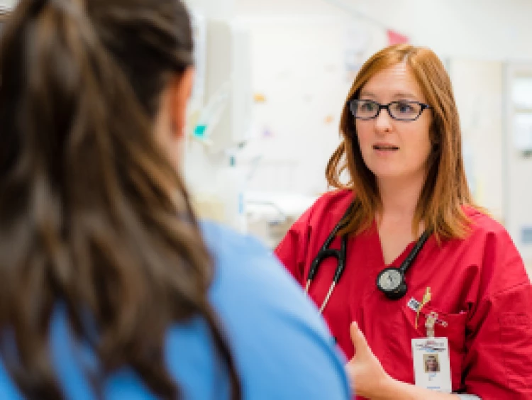 A House Officer in red scrubs having a discussion with a nurse in the patients' ward