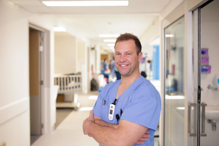 Critical Care Specialist standing with his arms crossed smiling in the hospital corridor