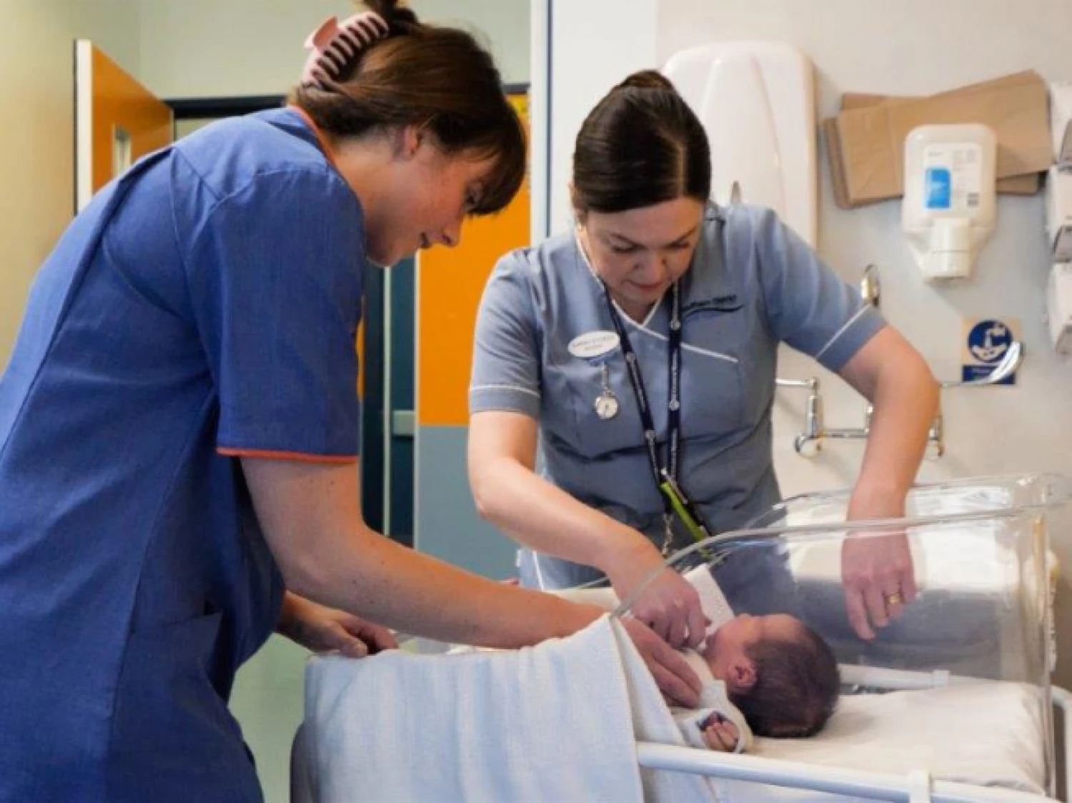 A midwife and a paediatric nurse conducting a regular health check on a newborn baby in the maternity ward.