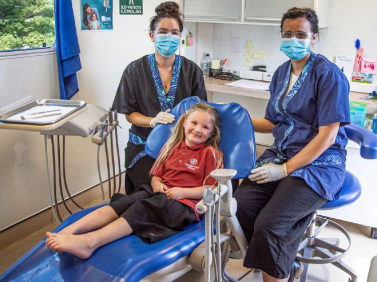 Two Oral Health Therapists sitting on either side of a primary school aged patient for her dental treatment.