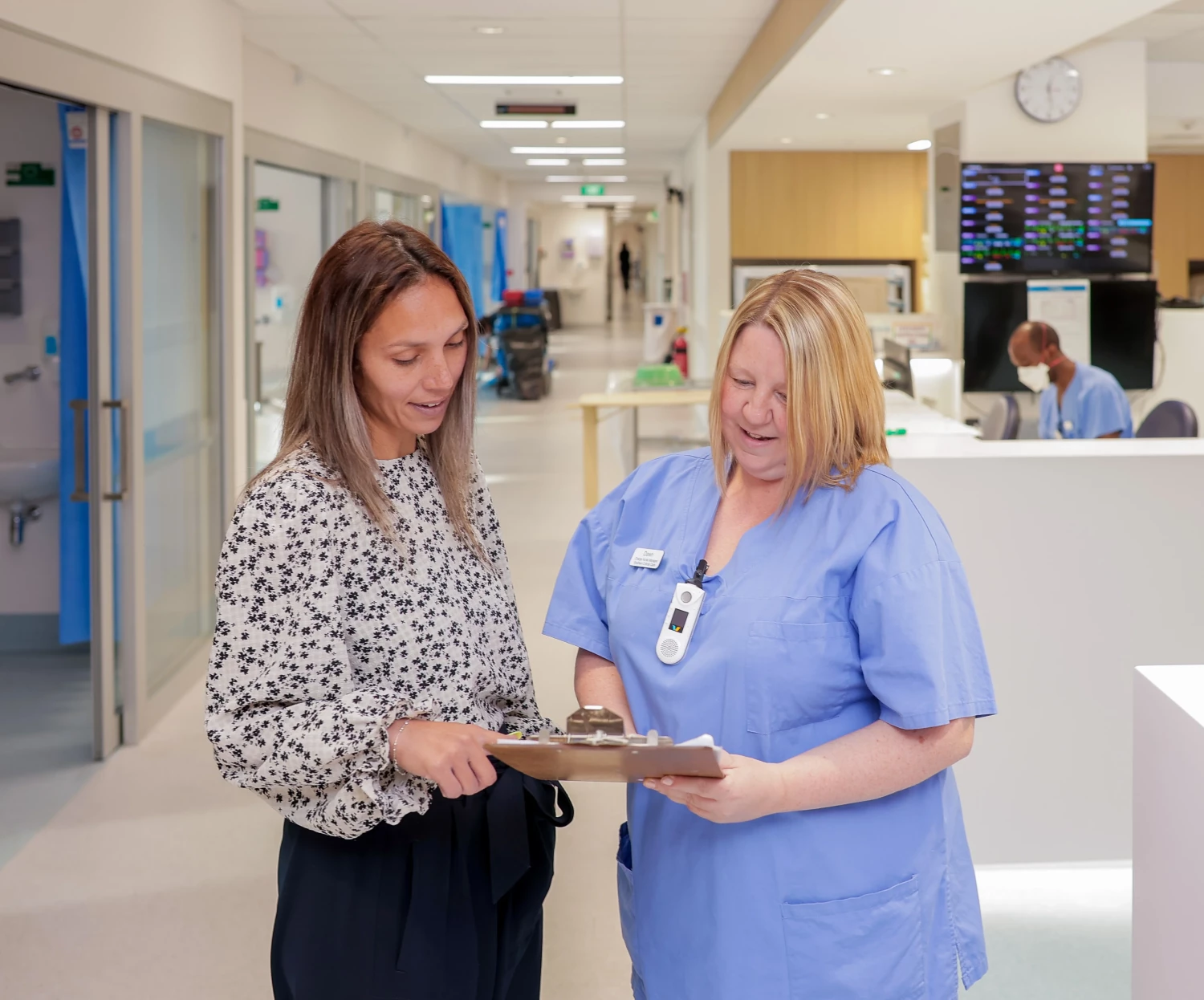 Critical Care Charge Nurse Dawn in light blue scrubs conversing with Tamara in the hospital corridor.