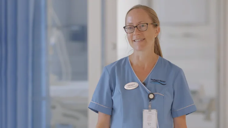 ICU nurse Wendy in light blue scrubs standing in a hospital ward.