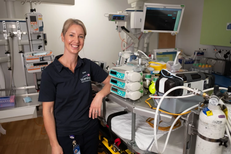PICU Transport Nurse Zoe standing next to and learning on a table with hospital equipment.